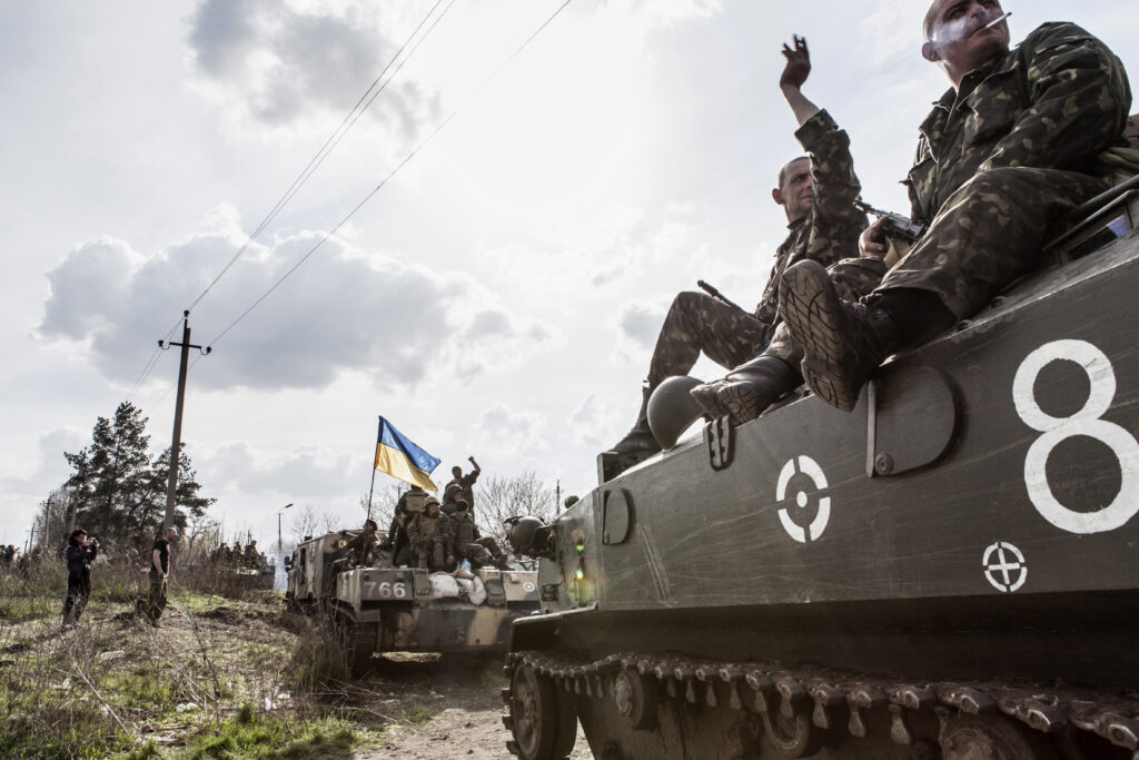 Ukrainian troops sit on two armoured vehicles travelling through Donbas. One vehicle is carrying a Ukrainian flag