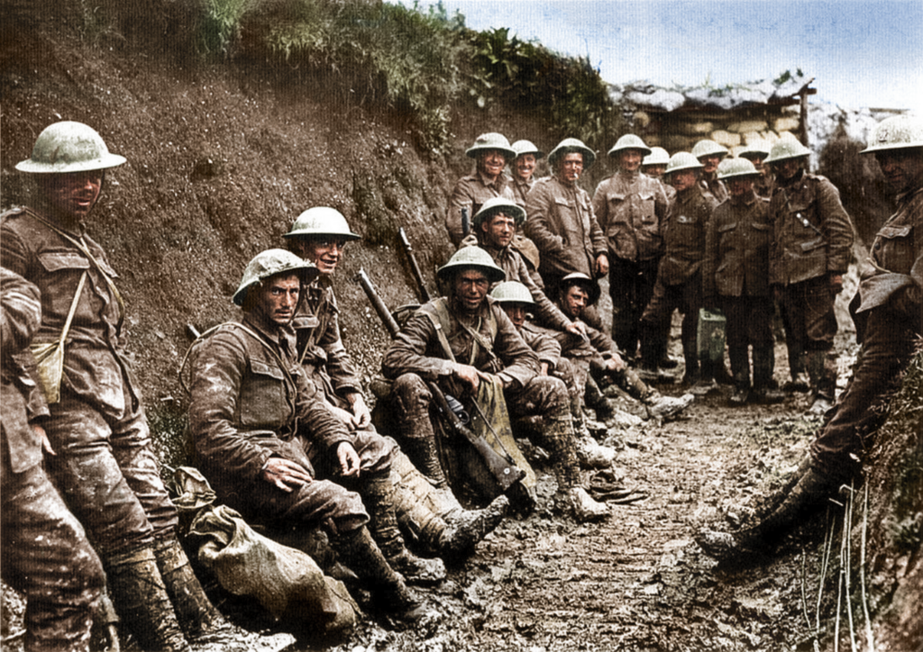 A colourised photograph showing mud-covered men leaning against the walls of a deep trench.