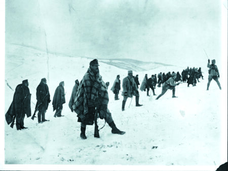 Hungarian troops wrapped in rudimentary winter clothing stand in a horizontal line. In front, an officer waves his sword to order the advance