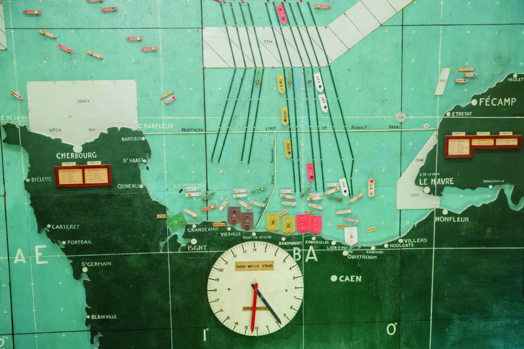 A map of Normandy and the English channel, with a clock at the bottom and model ships positioned.