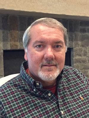 A portrait photograph of Mark Stille. He is wearing a red and green checked shirt.