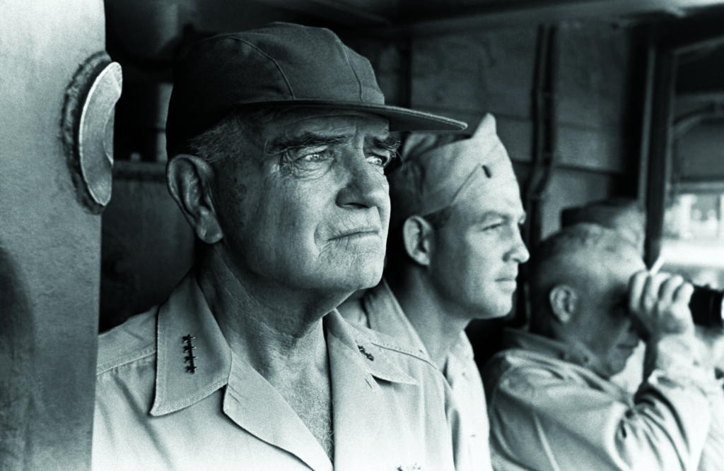 Halsey wears a cap and military uniform and stares out to sea.