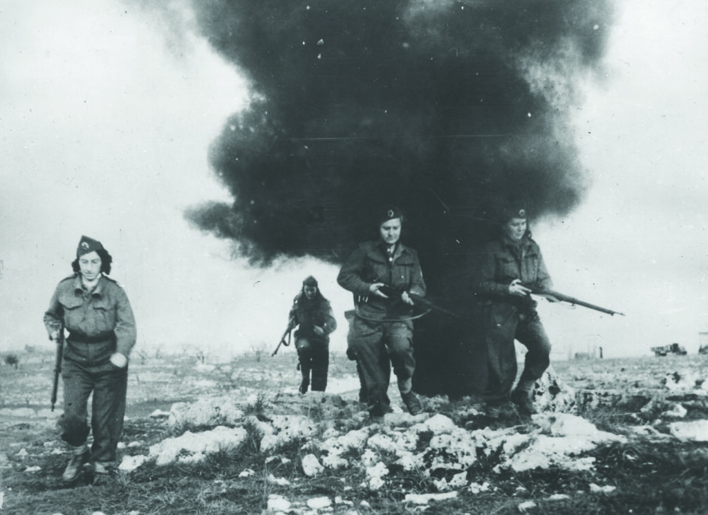 Four female partisans walk through smoke while carrying rifles
