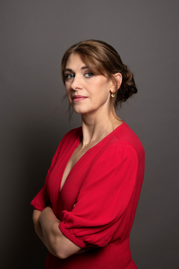 A portrait photograph of Clare Mulley, wearing red against a grey background