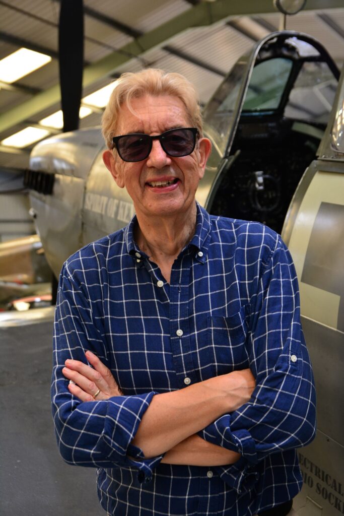 A portrait photograph of Paul Beaver. He has his arms crossed and is standing in front of an aircraft.